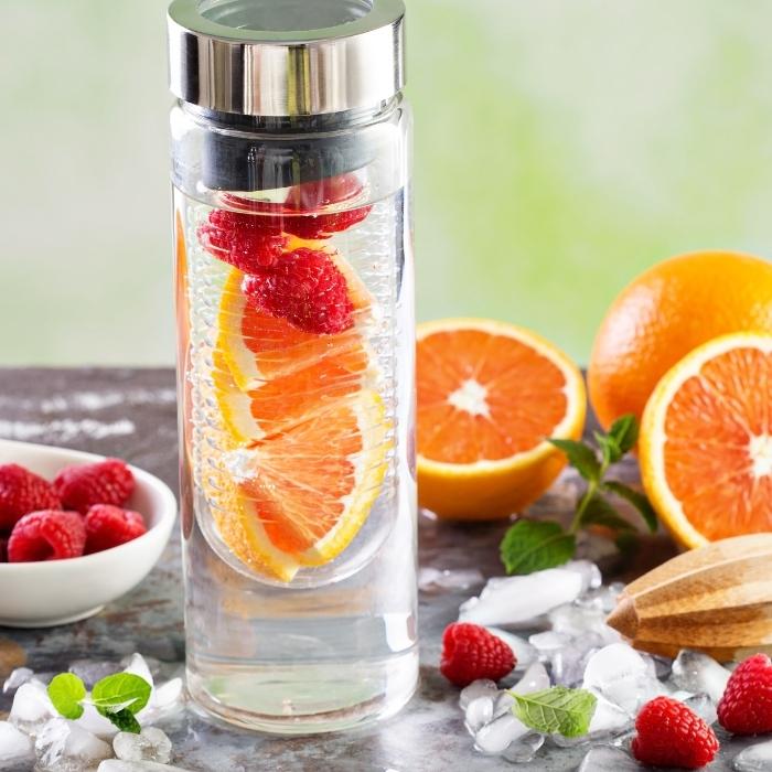 Glass jar with water infused with orange slices and raspberries.