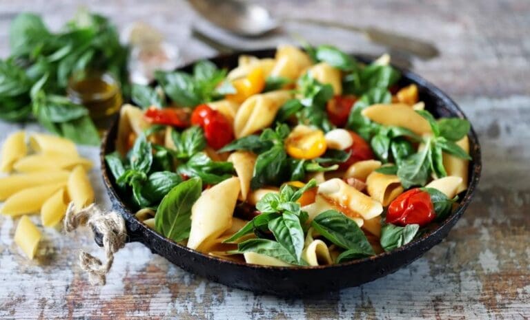 Pasta in a shallow bowl with olive oil, tomatoes, and fresh basil.