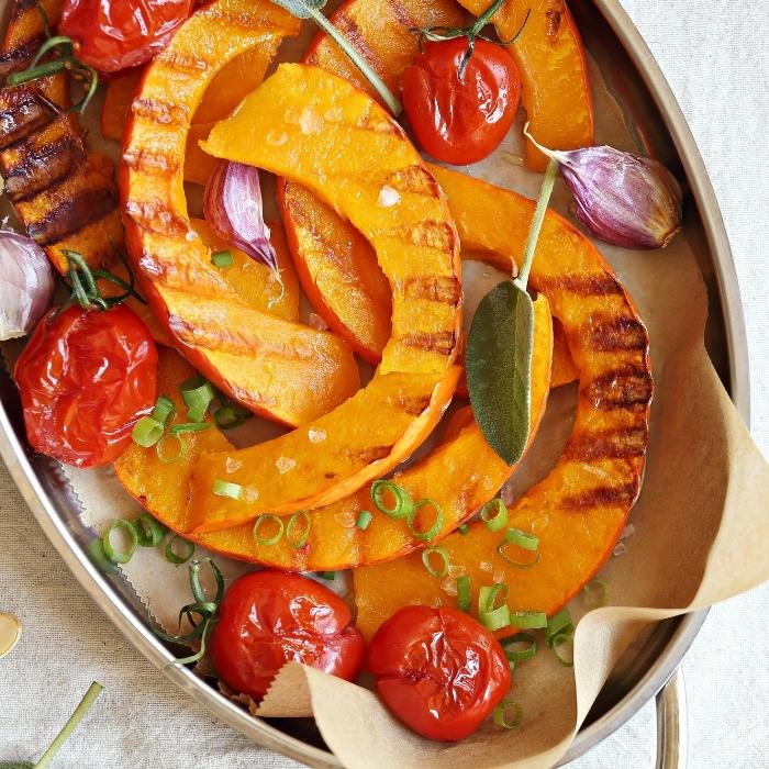 Slices of grilled pumpkin in a dish with tomatoes, sage, garlic, and chives.