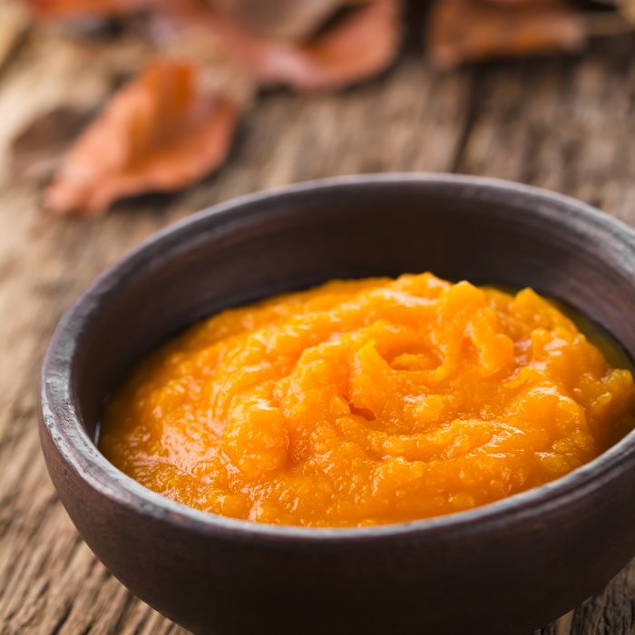 Bowl of pumpkin puree on wooden tabletop.
