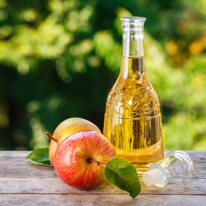 A glass bottle of apple cider vinegar next to some apples.