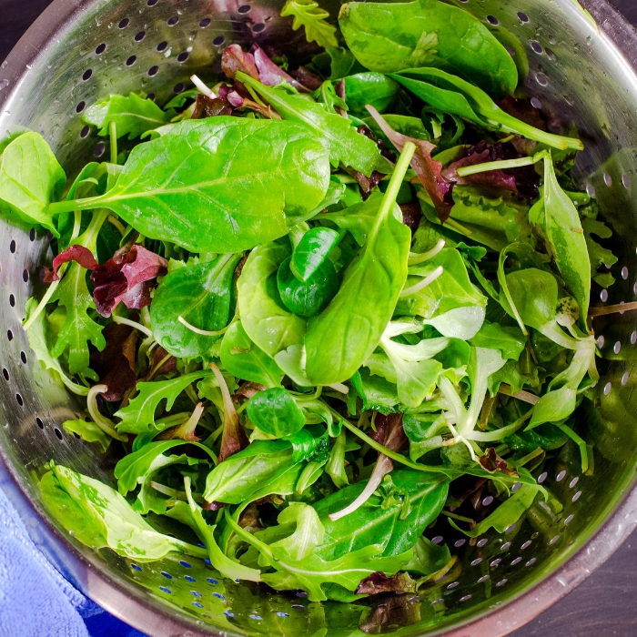 A variety of fresh salad greens in a colander.