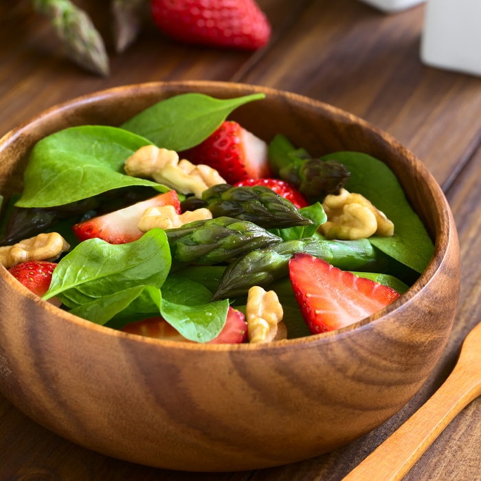 Strawberry, asparagus, baby spinach, and walnut salad in a wooden bowl.