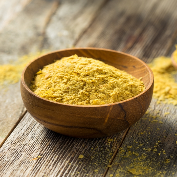 A wooden bowl of nutritional yeast on a table top.