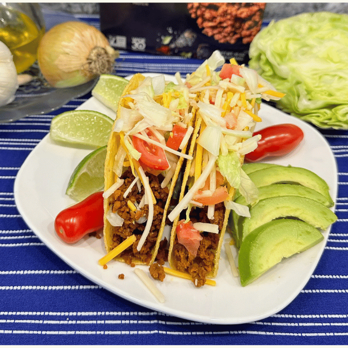 Abbot's Chorizo in tacos on a white plate with lettuce, tomatoes, and shredded vegan cheese.